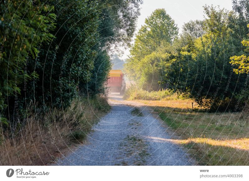 Ein Traktor fährt auf einem staubigen Feldweg mit einem Heuwagen durch Büsche zu einer Wiese Straße Sträucher Textfreiraum unbefestigter Weg Laufwerk Landwirt