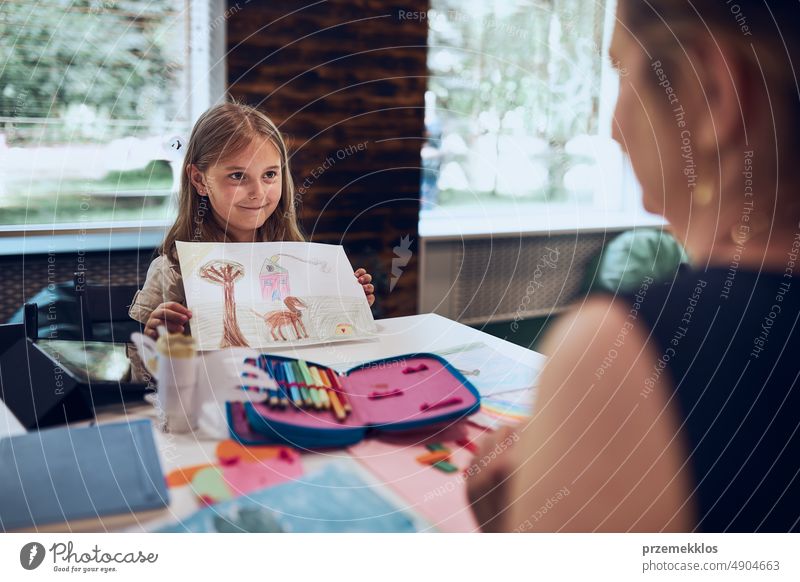 Mädchen präsentiert ihr Kunstwerk Lehrer. Frau unterstützt Schülerin während des Unterrichts in der Grundschule. Kind zeichnet Bild am Schreibtisch sitzend im Klassenzimmer. Lernen in der Grundschule. Zurück zur Schule