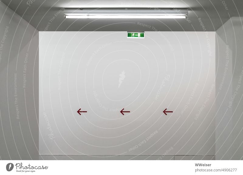Die Pfeile zeigen nach links, der Notausgang ist rechts, aber ist das nicht eine Sackgasse? Ausgang Weg Wegweiser dalang entlang weisen Richtung Raum dahinter