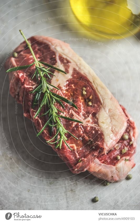 Nahaufnahme eines rohen Rindersteaks mit Rosmarin und Olivenöl am grauen Betonküchentisch. abschließen Küchentisch Metzger Hintergrund frisch Rindfleisch