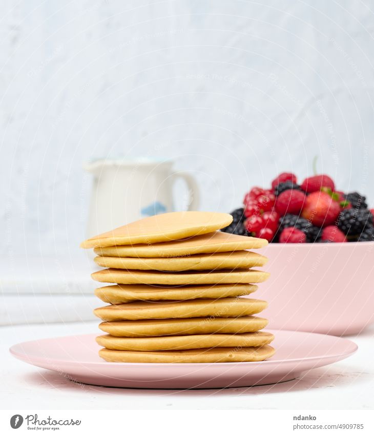 Stapel von gebackenen Pfannkuchen mit Früchten in einem runden Teller auf einem weißen Tisch schwarz Zucker Frühstück Lebensmittel süß Mahlzeit selbstgemacht