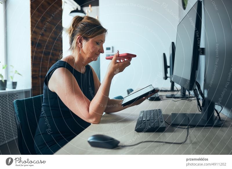 Geschäftsfrau mit Geschäftsanruf arbeiten auf Tablet im Büro. Reife beschäftigte Frau mit Touchpad-Computer stehend am Fenster in modernem Interieur Smartphone