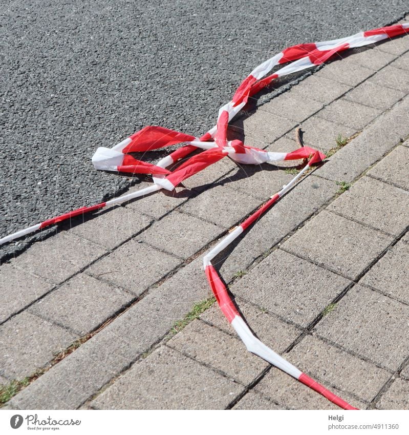 abgerissenes rot-weißes Absperrband liegt am Boden auf Pflastersteinen und Asphalt Flatterband Absperrung zerrissen zerstört kaputt Schutz Sicherheit Barriere