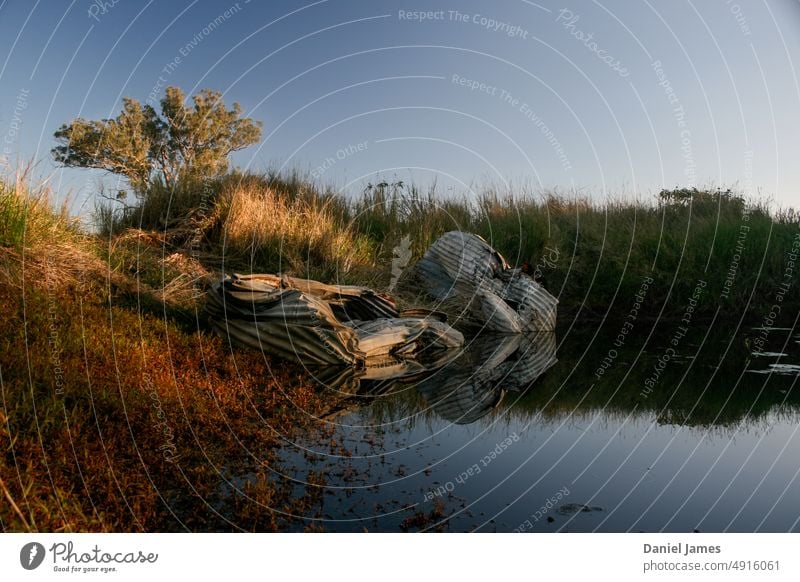 Zerknitterte Wassertanks aus Wellblech, die von einem Staudamm verlassen wurden. Damm See Teich Wellblechbehälter Bauernhof ländlich zerdrückt Schiffswrack