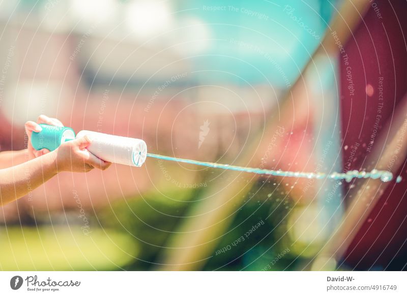 Kind spritzt mit einer Wasserpistole im Sommer Spaß nass Spaß haben Freude spielen Garten Hände Freizeit Kindheit