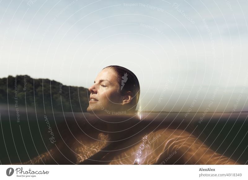 Junge, schöne Frau im flachen Wasser in der Ostsee schaut zur Seite und lächelt - Sichtbarkeit Teil- Unterwasserbild Lifestyle Gegenlicht gesund sportlich