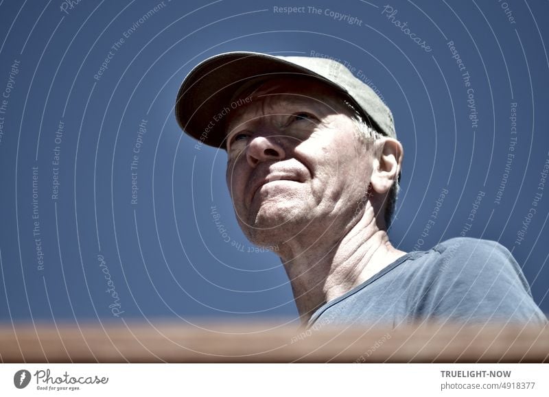 Weg und Ziel konzentriert im Blick: Mann mit Basecap vor wolkenlosem blauen Himmel, Sonnenlicht und Schatten im Gesicht, blaugraues T-Shirt, Portrait, untersichtig aufgenommen