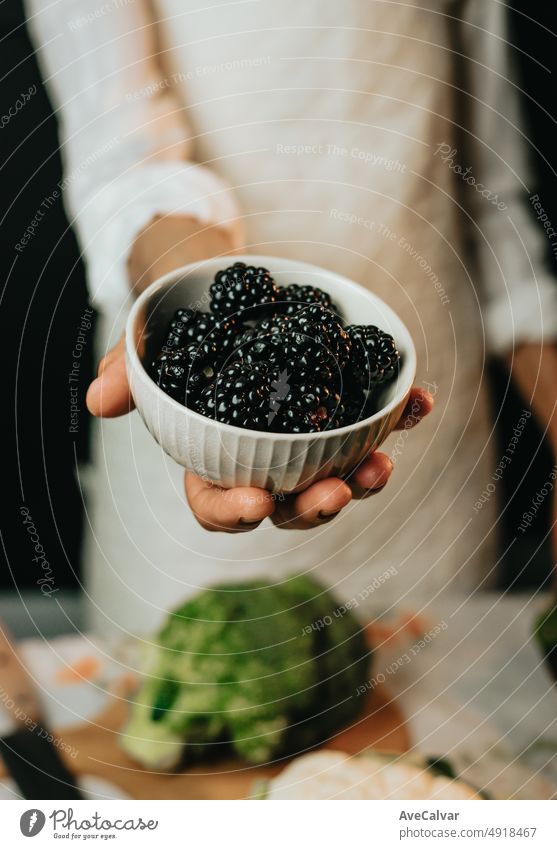 Close up Bild einer alten Frau Kochen Koch packt Brombeere bietet der Kamera vor der Vorbereitung sie in einem gesunden food.Rustic Küche Kochen von Koch gemacht. Die Vorbereitung Zutat für eine Bio-Mahlzeit.