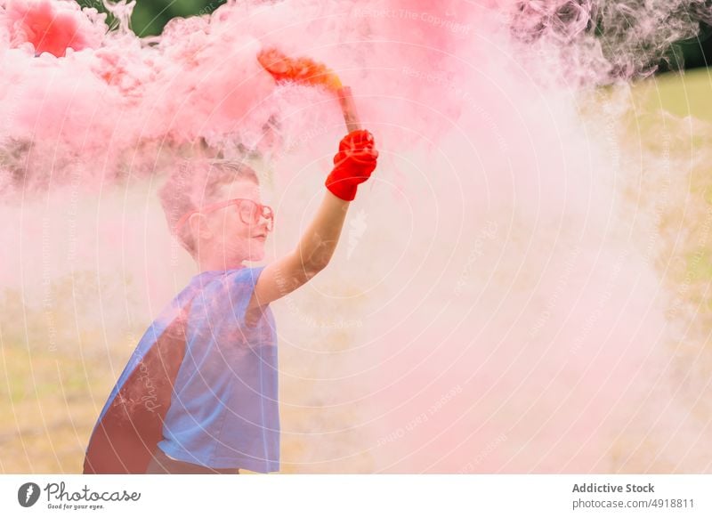 Kleiner Superheld mit Rauchbombe Junge Park Tracht spielen Kraft Fokus Rasen farbenfroh hell Kind Vorstellungskraft Phantasie bezaubernd Sommer pulsierend