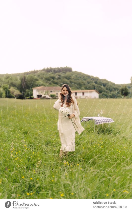 Lächelnde Frau mit Blumen im Feld stehend Blumenstrauß Landschaft Gras Erholung Sommer Haufen Natur Zeitvertreib feminin Tisch Freude geblümt Pflanze Umwelt