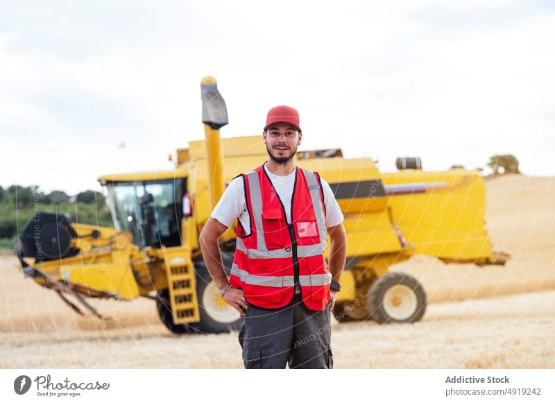 Mann steht auf einem Feld mit Mähdrescher Landwirt Arbeiter Erntemaschine Ackerbau Landschaft Porträt Schonung industriell Job Wehen Beruf Weizen Vollbart