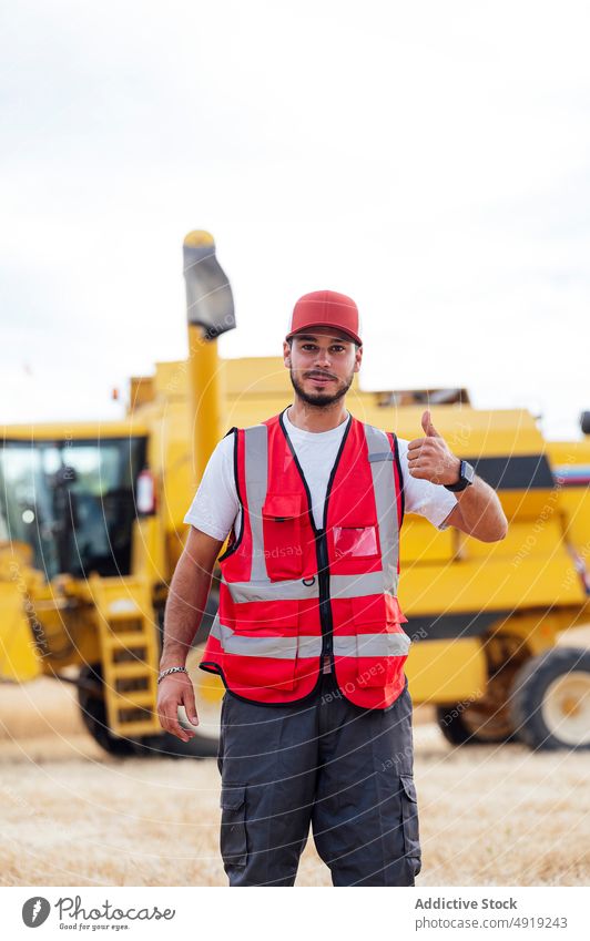 Mann macht Daumen-nach-oben-Geste in der Nähe des Mähdreschers Arbeiter Daumen hoch mögen Landwirt Erntemaschine Ackerbau Landschaft Feld Agronomie Job gut