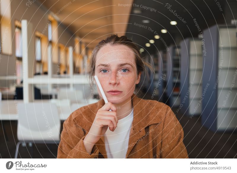 Junge Frau studiert in der Bibliothek Schüler lernen Bildung Hausaufgabe Gesicht berühren Schreibstift Universität Porträt jung forschen Hochschule ernst