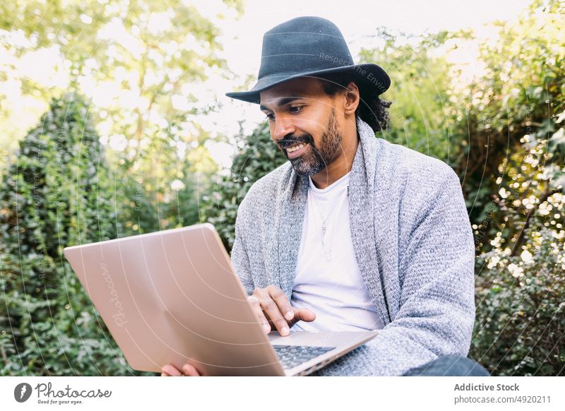 Stilvolle hispanische Freiberuflerin mit Laptop auf einer Bank Mann Surfen benutzend Park online abgelegen Projekt männlich freiberuflich Streetstyle