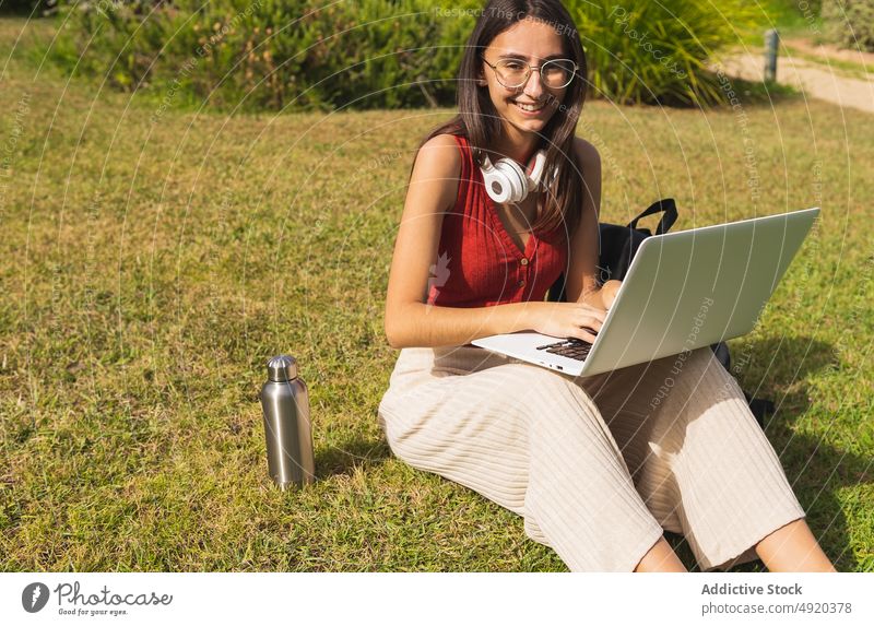 Frau studiert am Laptop im Park Schüler Rasen Hausaufgabe in die Kamera schauen Bildung Wissen lernen online Browsen Tippen Großstadt Netbook schulisch Straße