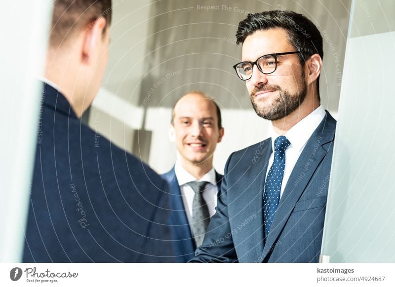 Gruppe von zuversichtlichen Geschäftsleuten, die sich bei einem Geschäftstreffen in einem modernen Büro mit einem Händedruck begrüßen oder eine Vereinbarung durch Schütteln der Hände abschließen.