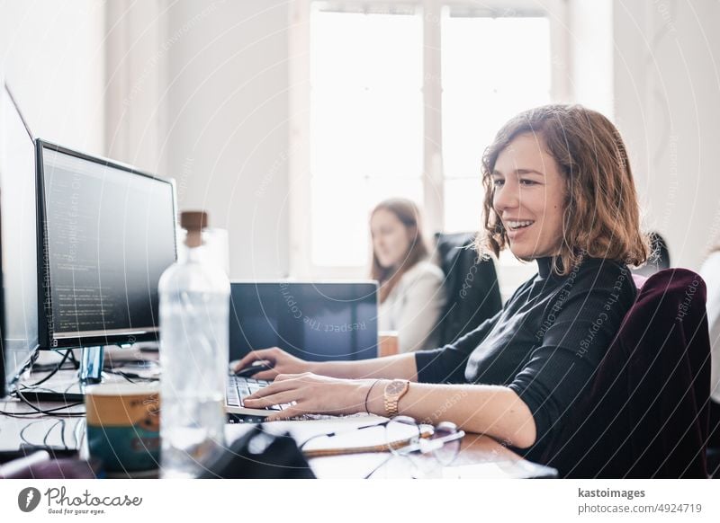 Frauen in Startup-Unternehmen und Unternehmertum. Junge engagierte weibliche KI-Programmiererinnen und IT-Softwareentwicklerinnen programmieren gemeinsam an einem Desktop-Computer in einem gemeinsamen Büro eines Startup-Unternehmens.