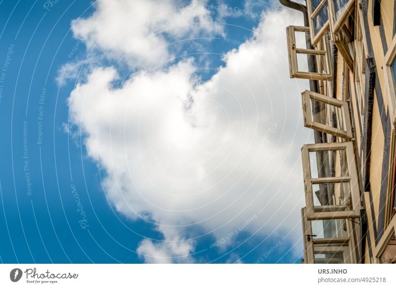 Eine große weiße Wolke am Himmel hinter der Fasade eines Fachwerkhauses - die Sprossenfenster  sind geöffnet, als scheinen sie den Sommer einfangen zu wollen - viel Freifläche für Text