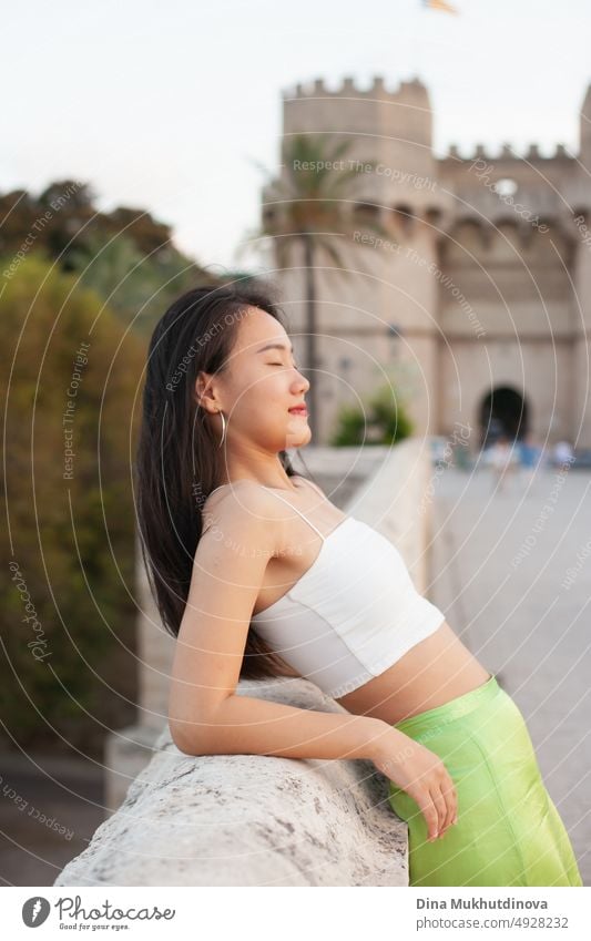 Schöne junge asiatische Frau auf der Straße einer historischen europäischen Stadt. Weibliche Touristin aus China auf Reisen in Europa, lächelnd. Austauschstudentin.