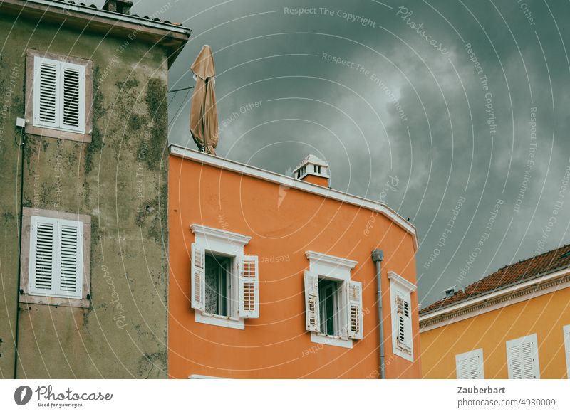 Fassaden mit weißen Fensterläden in dunkelgrau, orange und ocker vor dramatischen Wolken Fensterladen gestrichen Himmel Gewitter Haus Mauer Gebäude renovieren