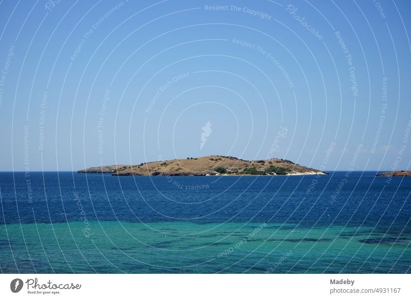 Blaues Wasser im Sommer bei blauem Himmel und Sonnenschein mit kleiner Insel vor einer Bucht in Foca am Ägäischen Meer in der Provinz Izmir in der Türkei