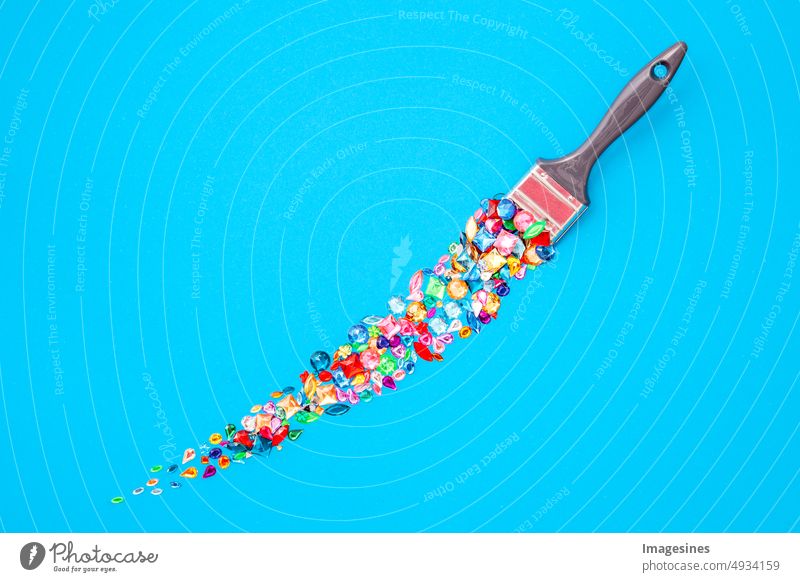 Künstlerisch zusammengesezte Edelsteine. Kreatives Layout aus mehrfarbigen Glassteinen und Pinsel, Pinselstrich isoliert auf blauem Hintergrund. Minimale kreative Flachlage. Ansicht von oben