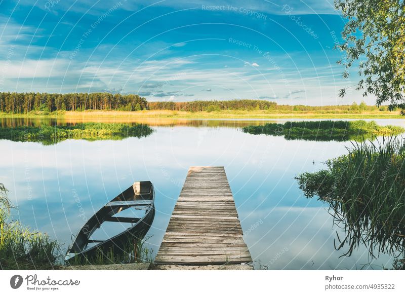 Alte hölzerne Fischerboot in der Nähe Pier im Sommer See oder Fluss. Schöner Sommer sonnigen Tag oder Abend. Verlassenes Boot. Russische Natur schön