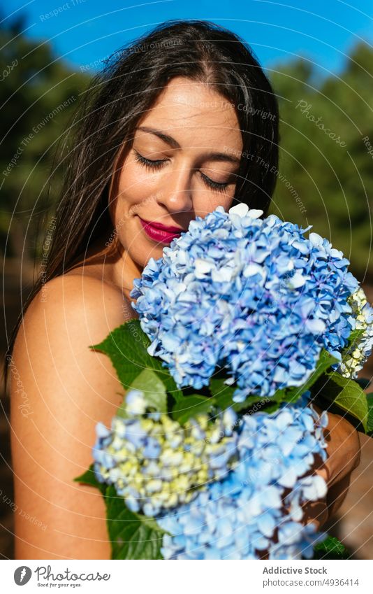 Glückliche, verführerische Dame mit einem Strauß zarter Hortensienblüten im Park Frau Blume Lächeln oben ohne Deckbrust feminin positiv sanft Augen geschlossen