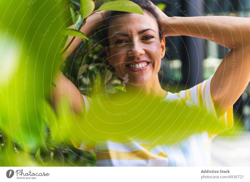 Positive Frau macht Pferdeschwanz auf der Straße Großstadt Frisur Buchse Pflanze Park Vorschein feminin Sommer heiter Lächeln grün positiv lässig Stil