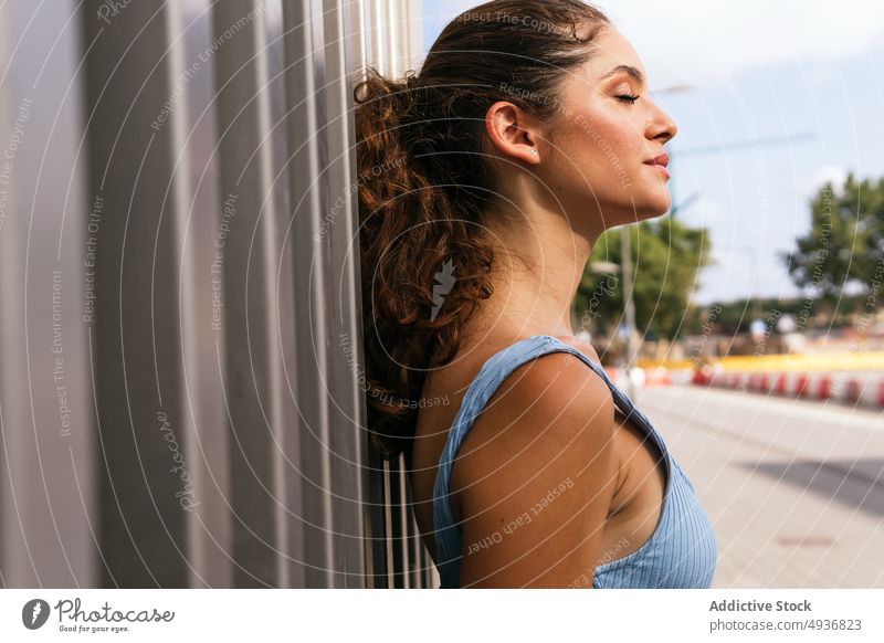 Coole junge Frau steht in der Nähe der Wand auf der Straße im Sonnenlicht selbstsicher selbstbewusst Stil Vorschein Porträt Persönlichkeit tausendjährig cool