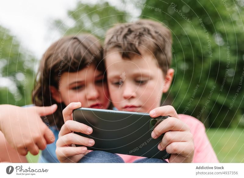 Geschwister nutzen Smartphone gemeinsam im Park Kinder Geschwisterkind Videospiel spielen Zusammensein Wochenende teilen Freundschaft Rasen Zeitvertreib online