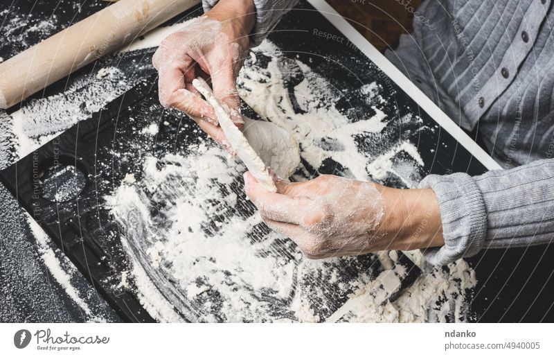 zwei Frauenhände kneten den Teig aus weißem Weizenmehl auf einem schwarzen Tisch, Draufsicht Mehl Hand Teigwaren Essen zubereiten Küche Lebensmittel Bäckerei