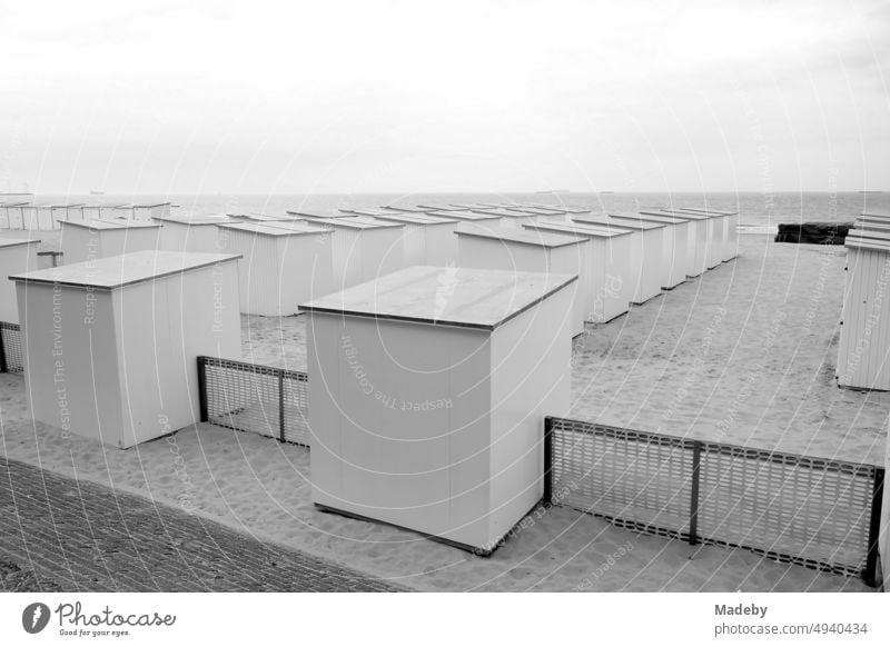 Lange Reihe mit traditionellen Strandkabinen bei Regenwetter am Strand in Knokke-Heist an der Nordsee bei Brügge in Westflandern in Belgien, fotografiert in klassischem Schwarzweiß