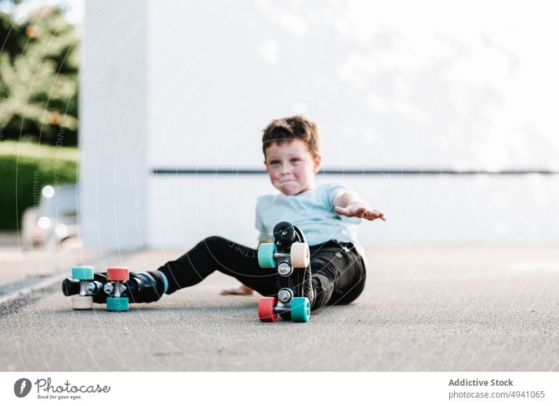 Junge in Rollschuhen auf dem Boden sitzend Rollerskate Pause Straße Wand Hobby Sommer Aktivität Kind lässig ruhen sich[Akk] entspannen tagsüber Kindheit