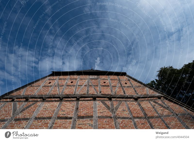 Blick nach oben entlang eines alten Fachwerkhauses mit roten Ziegeln bei leicht bewölktem Himmel Aufblick altes Haus Backsteinhaus Holzbalken blauer Himmel