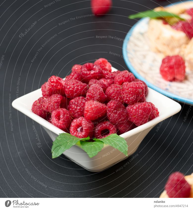 Reife rote Himbeeren in einer weißen Keramikschale auf einem schwarzen Tisch Beeren roh reif süß geschmackvoll Vegetarier Vitamin ganz hölzern Holzplatte essen