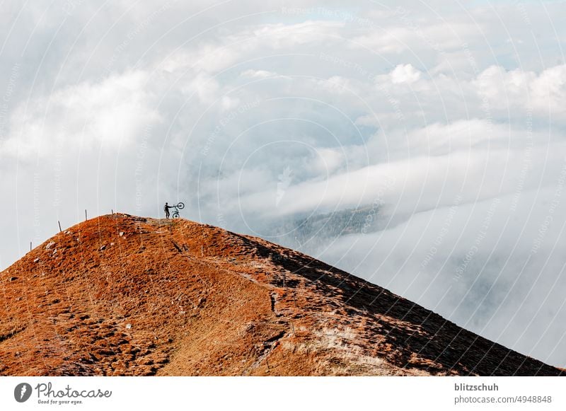 Mountainbiker in den Schweizer Alpen im Herbst geniesst das spezielle Wolken Panorama auf dem Gipfel abenteuer berge outdoor outdoor sport Radsport Sport Dunst