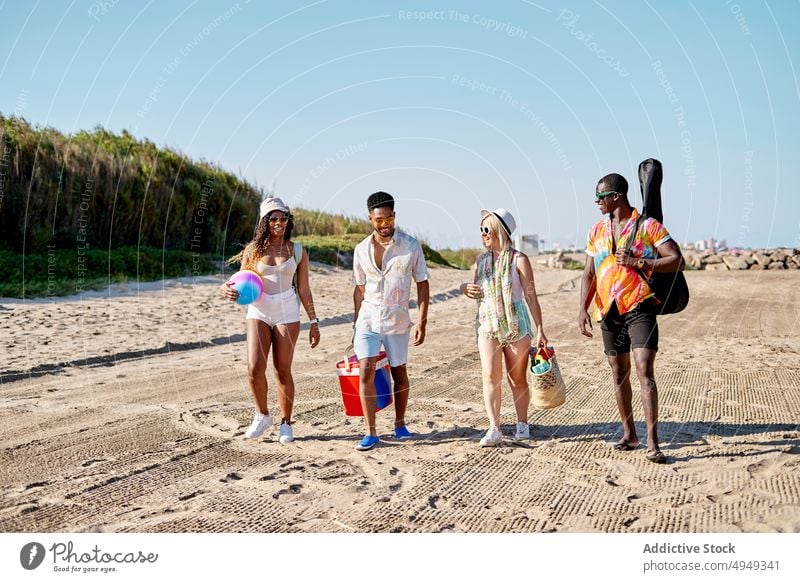 Glückliche Freunde am Strand Spaziergang Lächeln Sommer Wochenende Zusammensein Sand Blauer Himmel Resort tagsüber Männer froh Frauen jung Freude schlendern