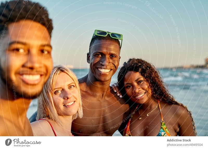 Multiethnische Freundinnen und Freunde umarmen sich am Meer bei Sonnenuntergang Umarmung MEER winken Lächeln Wolkenloser Himmel Strand Zusammensein Porträt