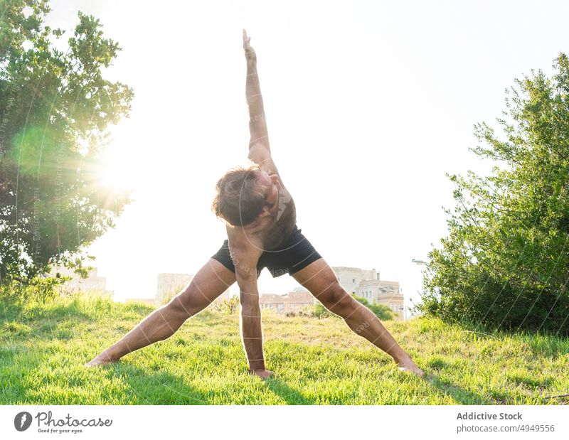 Mann beim weitbeinigen Vorwärtsbeugen Twist Dehnung Rasen beweglich Yoga Morgen Park Sommer üben männlich Zen Asana Gras ohne Hemd Energie Achtsamkeit Wellness