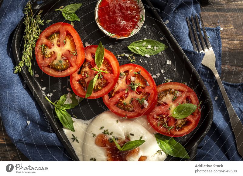 Leckeres Gericht mit Tomaten, Käse und Kräutern auf dem Tablett Burrata Saucen Basilikum Thymian Mozzarella lecker Gemüse Kraut appetitlich Stoff Salz Gabel