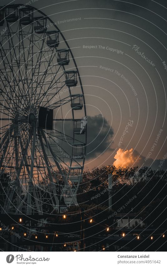 Riesenrad vor Abendhimmel mit von der Sonne angestrahlten Wolken. Jahrmarkt Himmel Licht dunkel düster Fahrgeschäfte Nacht Sonnenuntergang