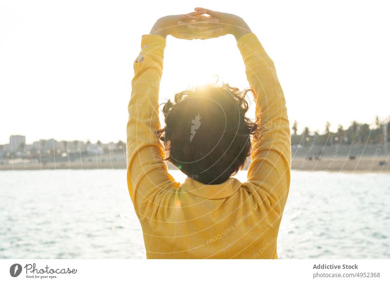 Anonyme Frau mit erhobenen Händen an der Strandpromenade Freiheit genießen Großstadt Sonnenuntergang Arme hochgezogen Windstille Inspiration Harmonie Ufer MEER