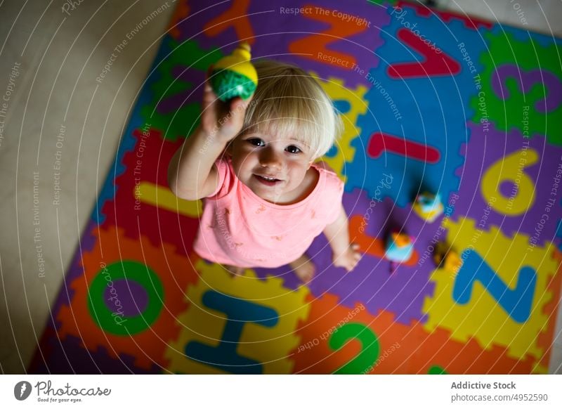 Mädchen spielt auf Fußmatte Kind in die Kamera schauen spielen Draufsicht Spielteppich Spielzeug wenig unterhalten Kleinkind Stock bezaubernd Matten heimwärts