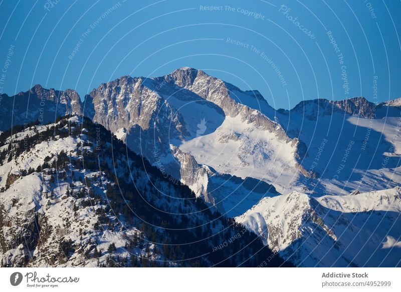 Mit Schnee bedeckter Berghang unter blauem Himmel Berge u. Gebirge steil Felsen Baum Hochland Stein Natur kalt Tierwelt Gipfel Blauer Himmel Umwelt Winter