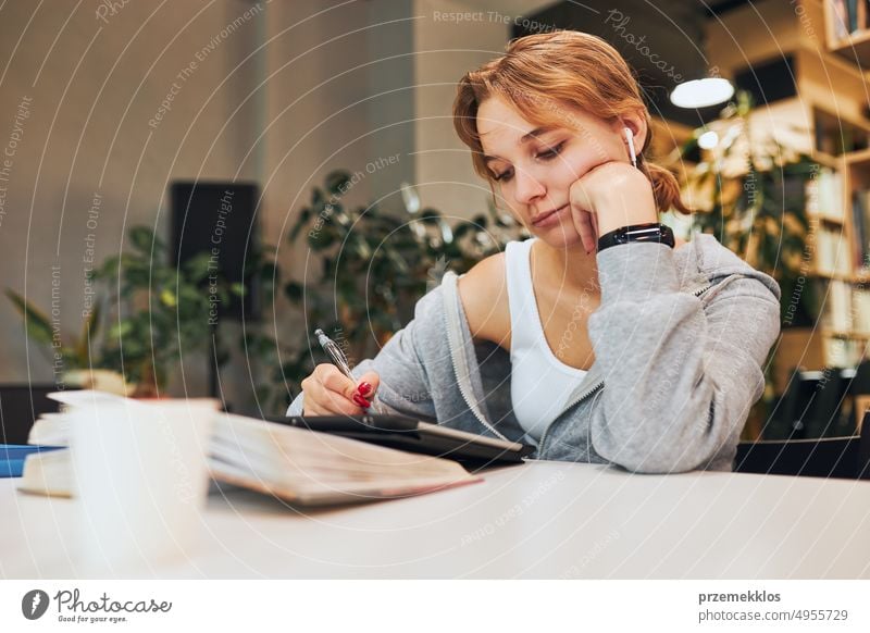 Studentin lernt in der Universitätsbibliothek. Junge Frau schreibt Aufsatz und macht Notizen mit Computer-Tablet. Konzentrierter Student, der für College-Prüfungen lernt