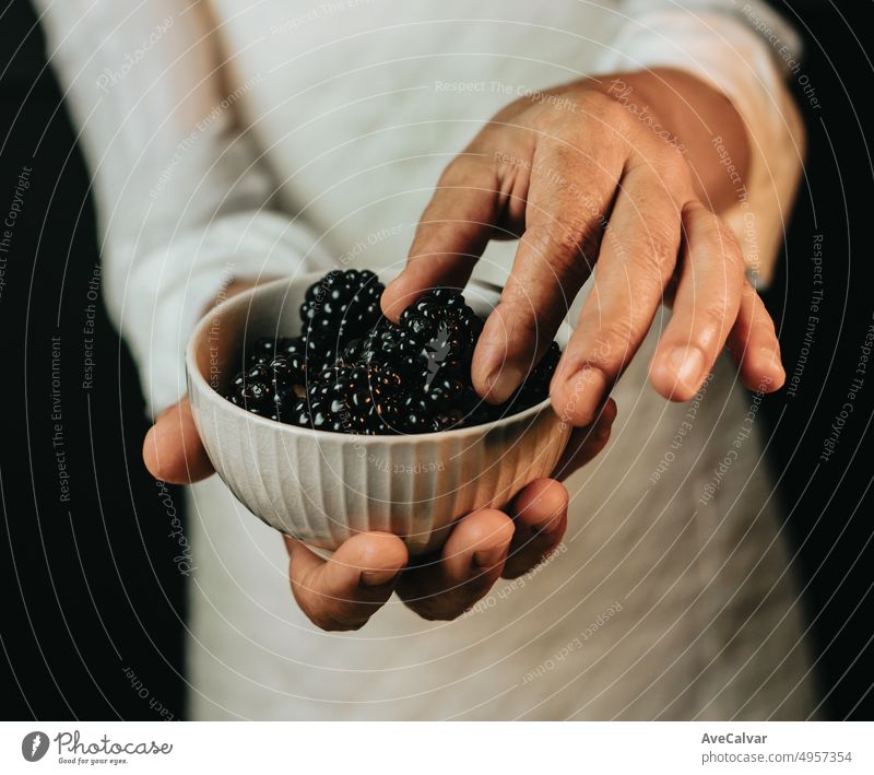 Nahaufnahme von Händen, die eine Schüssel mit Brombeeren halten, die die erforderliche Menge für das Rezept eines Desserts zeigen, das eine gesunde und süße Mahlzeit für Frühstück, Brunch oder Nachmittagssnack zubereitet