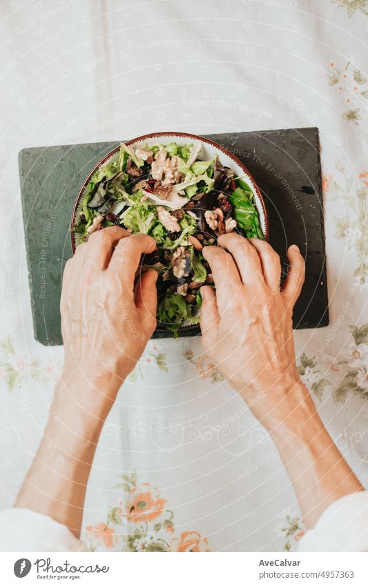 Oma, die ein gesundes Rezept mit faltigen Händen fertigstellt, um es in die Netzwerke hochzuladen.Salat mit Salat, Nüssen, Walnüssen, Rosinen und Mandeln in einer Schüssel auf einem schwarzen Brett.Perfektes Rezept für die Begleitung einer Diät