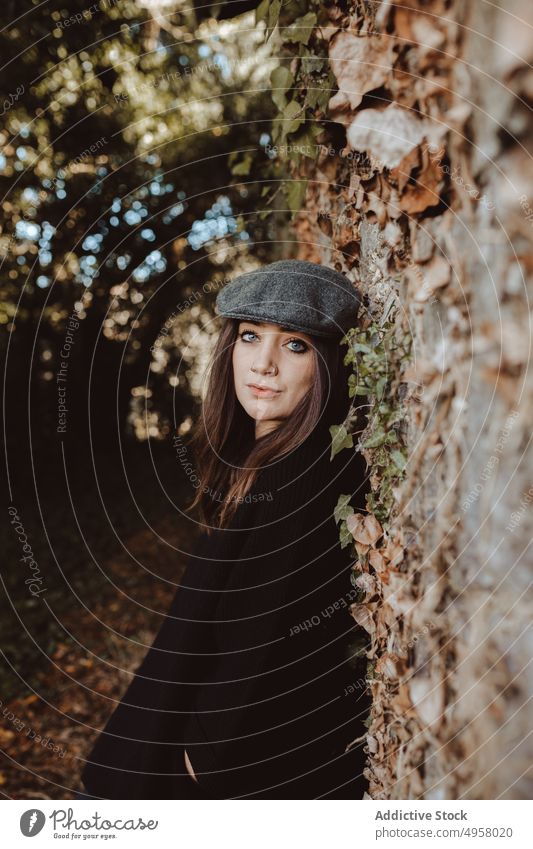 Trendy Frau steht in der Nähe der Wand im Herbst Park gealtert Lehnen Stil sonnig tagsüber in die Kamera schauen Lifestyle Freizeit ruhen sich[Akk] entspannen