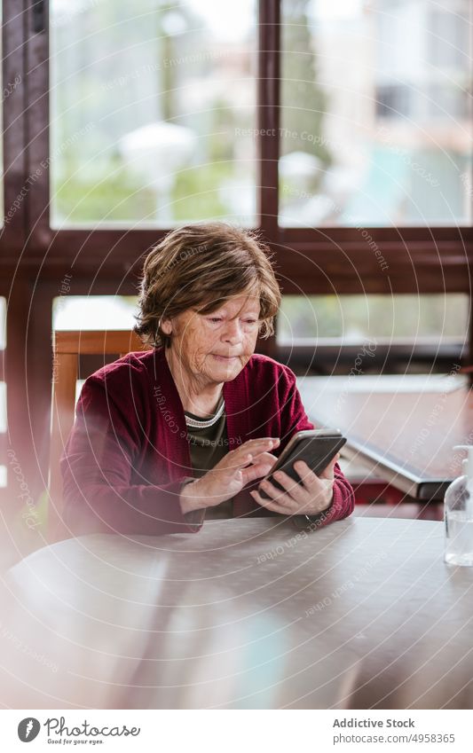 Ältere Frau mit Smartphone am Tisch benutzend heimwärts älter soziale Netzwerke sitzen ruhen Rentnerin Senior Brille Browsen Gerät Apparatur Internet online